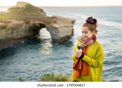 Beautiful Asian Woman With Coffee Cup During Sunrise At Tunnel Beach, Otago Peninsula, New Zealand.