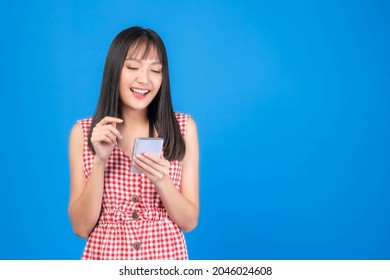 Beautiful Asian Woman Cute Girl Bangs Hair Style In Red Dress Playing A Smart Phone Isolated On Blue Background - Mobile Phone Uses A Online Banking For Pay Online Shopping