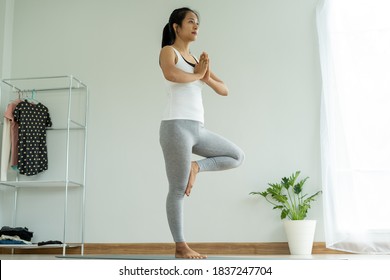 Beautiful Asian woman doing yoga at home. Women maintain balance in a tree pose and practice breathing in and out slowly. Health and fitness concept