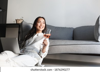 Beautiful asian woman drinking wine and using laptop, sitting on floor and resting at home. - Powered by Shutterstock