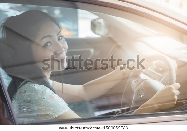 beautiful Asian woman drives a car with a\
glass door in the\
background