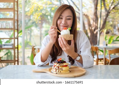 A beautiful asian woman eating ice cream with a mixed berries pancakes and whipped cream by wooden spoon - Powered by Shutterstock