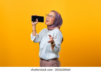 Beautiful Asian Woman Enjoying Singing Using Smartphone Over Yellow Background