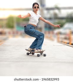 Beautiful Asian Woman Enjoys Balancing Skateboard On City Street. Young Female Teen Skater Practices Surf Skate Board Exercise In Urban Road. Skateboarding Is A Trendy Outdoor Action Sport In Thailand