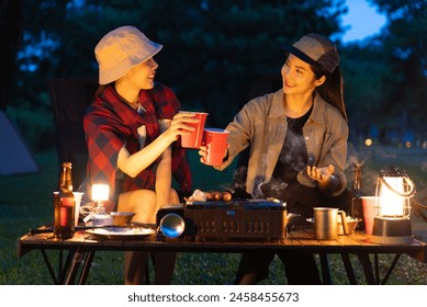 Beautiful asian woman friends enjoy drinking a beer and grilling meat together. They feeling exited while camping in the nature at night. Recreation and journey outdoor activity lifestyle. - Powered by Shutterstock