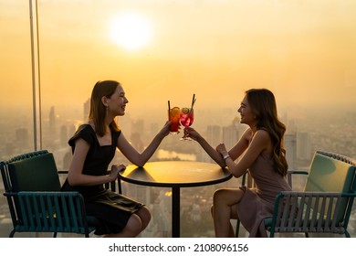 Beautiful Asian woman friends meeting and drinking cocktail together at skyscraper rooftop restaurant in metropolis at summer sunset. Female friend enjoy outdoor lifestyle in the city at night - Powered by Shutterstock