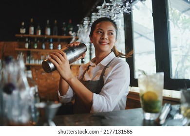 Beautiful Asian woman in gray apron preparing cocktail on the bar counter.