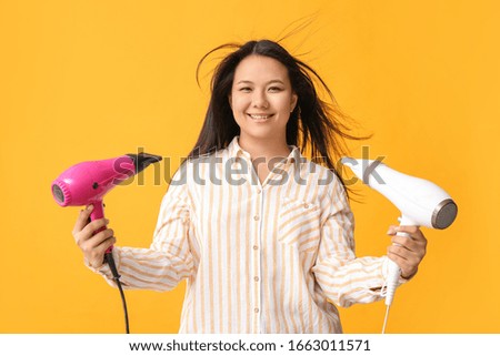 Beautiful Asian woman with hair dryers on color background