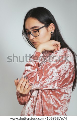 beautiful Asian woman has pain in the elbow joint, wears glasses and a pink sweater, studio photo on the background