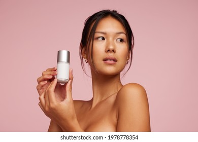 Beautiful Asian Woman Holding Beauty Care Product. Female Model Presenting Cosmetic Product And Looking Away.