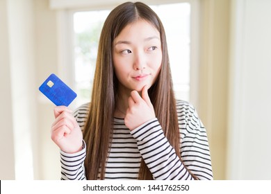Beautiful Asian woman holding credit card serious face thinking about question, very confused idea Stock Photo
