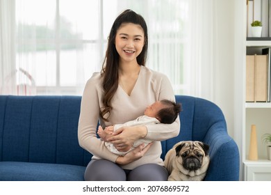 Beautiful Asian Woman Holding Newborn Baby In Her Arms Sit On Couch With Cute Dog Pug Breed At Cozy Home.Happy Infant Baby Sleep In Mother Arms Safety And Comfortable.Mom And Baby Concept