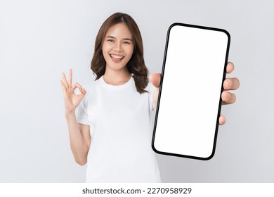 Beautiful Asian woman holding smartphone mockup of blank screen and shows ok sign on grey background. - Powered by Shutterstock