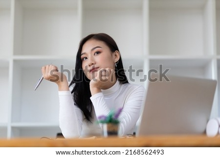 Beautiful Asian woman in the home office thinking and writing on a notepad.