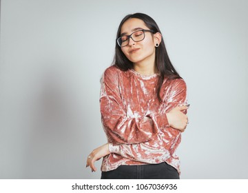 Beautiful Asian Woman Hugging Herself Cozy, Wearing Glasses And Pink Sweater, Studio Photo On Background