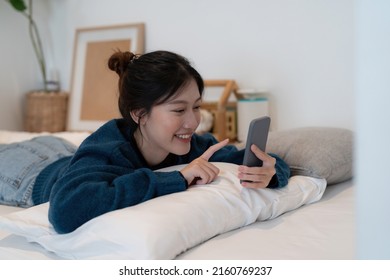 Beautiful asian woman laying down on white bed using mobile phone and smile in morning sunday.