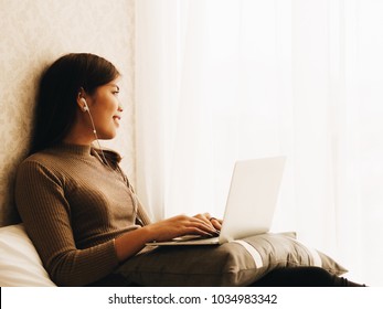 Beautiful Asian woman laying on sofa and using laptop working at her home. - Shutterstock ID 1034983342