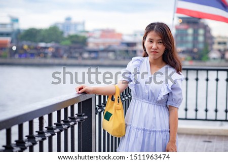Beautiful Asian woman in light blue dress carrying a small yellow tote bag standing at the riverside