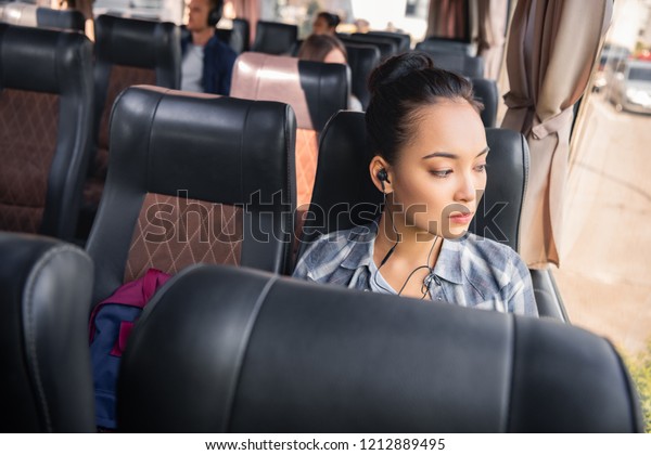 beautiful asian woman listening music in earphones\
during trip on travel bus\

