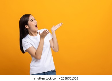 Beautiful asian woman look into blank space. Smiling female wearing white shirt on isolated yellow background. Attractive Teenager girl looking at empty space for text feeling excited and surprised.