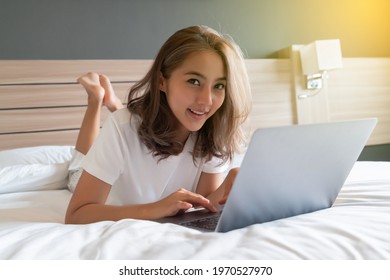 Beautiful Asian Woman Lying Down And Smiling The Bed And Her Laptop. WFH Working From Home In Quarantine Lockdown. Social Distancing Self Isolation