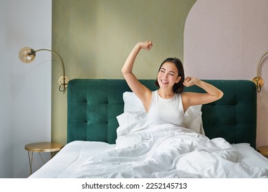 Beautiful asian woman lying in her bedroom on bed, stretching hands and looking outside, waking up from sleep. - Powered by Shutterstock