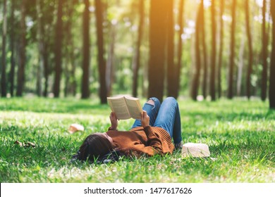 A beautiful Asian woman lying and reading a book in the park  - Powered by Shutterstock