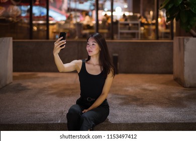 Beautiful Asian Woman Outdoors At Night Taking Selfie With Mobile Phone