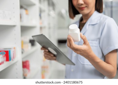 Beautiful asian woman pharmacist checks inventory of medicine in pharmacy drugstore. Professional Female Pharmacist wearing uniform standing near drugs shelves working with tablet. - Powered by Shutterstock