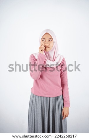 Beautiful Asian woman in pink sweater and headscarf showing crying expression with hand on cheek on white background