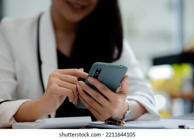 Beautiful Asian Woman Playing Mobile Phone In Her Break From Work, She Is A Marketing Manager Of A Startup Company, Female Leader, Supervisor, Ceo. Female Leadership Concept.