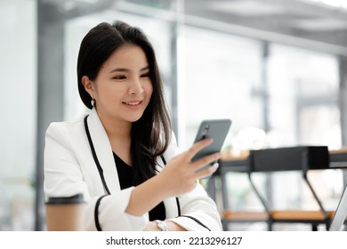 Beautiful Asian Woman Playing Mobile Phone In Her Break From Work, She Is A Marketing Manager Of A Startup Company, Female Leader, Supervisor, Ceo. Female Leadership Concept.