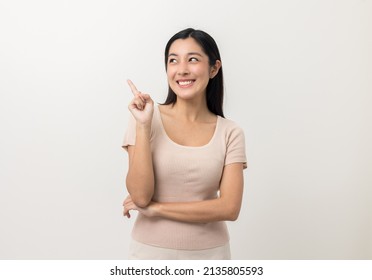 Beautiful Asian Woman Pointing Finger Into Blank Space. Smiling Female Standing Pose On Isolated White Background. Attractive Teenager Girl Around 25 Looking At Empty Space For Advertise Text.