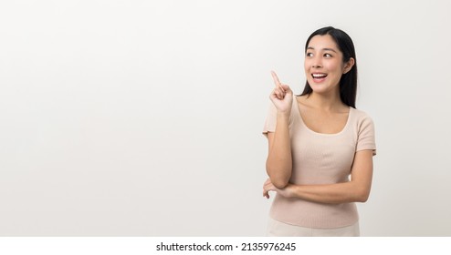 Beautiful Asian Woman Pointing Finger Into Blank Space. Smiling Female Standing Pose On Isolated White Background. Attractive Teenager Girl Around 25 Looking At Empty Space For Advertise Text.