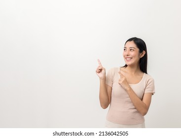 Beautiful Asian Woman Pointing Finger Into Blank Space. Smiling Female Standing Pose On Isolated White Background. Attractive Teenager Girl Around 25 Looking At Empty Space For Advertise Text.