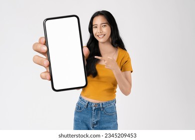 Beautiful Asian woman pointing finger on mobile and holding big smartphone mockup of blank screen on background.