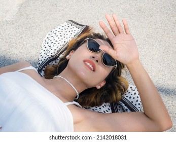 Beautiful Asian Woman Portrait In Casual White Shirt Wearing Sunglasses And Hair Scarf Looking Up And Shading Eyes With Her Hand On The Ground On Sunny Day In Summer.