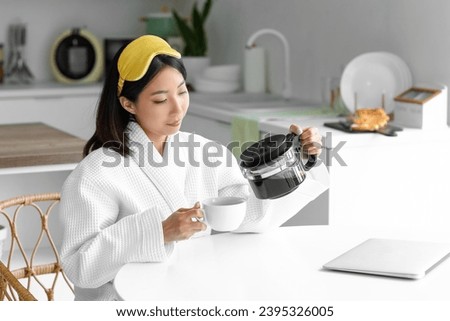 Beautiful Asian woman pouring coffee into cup in kitchen
