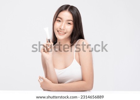 Beautiful Asian woman with a radiant smile holding a blank tube, ready for your cosmetic or skincare branding. Confidence and elegance personified isolated on white background. Self Care Concept