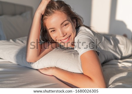 Beautiful Asian woman relaxing at home on pillow bed in bedroom candid smiling portrait. Natural beauty healthy skin model face.