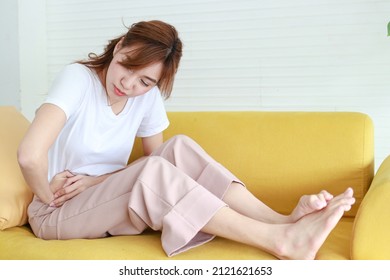 Beautiful Asian woman with right lower abdominal pain. She sits on the sofa at home. concept of appendicitis treatment The ureter and uterine lining in women. health care - Shutterstock ID 2121621653