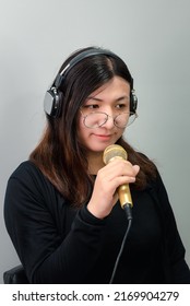 Beautiful Asian Woman Singer. She Enjoying Sing A Song Or Karaoke In Music Studio With Microphone Condenser And Headphones For Fun Or Voice Creative