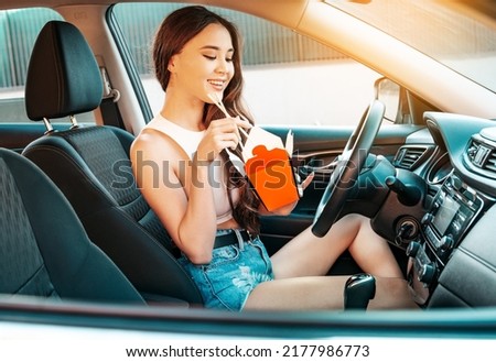 Beautiful asian woman sitting in the car and eating from wok box using chopsticks.