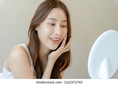 Beautiful Asian woman sitting in front of a mirror. face of a healthy woman applying cream and makeup. Advertisement for skin cream, anti-wrinkle cream, baby face
