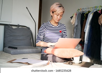 Beautiful Asian Woman Sitting On Bed & Working From Home On Laptop