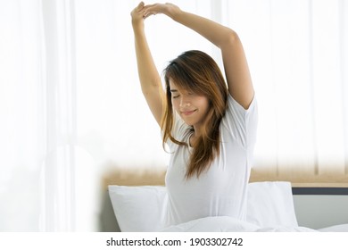 Beautiful Asian Woman Sitting On Bed And Stretch Lazily Oneself At Woke Up In Early Morning. Young Female Happy Resting In Cozy Bedroom At Home Then Cheerful Wake Up Smiling For New Day Good Life.