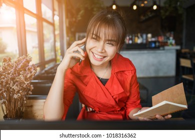 Beautiful Asian Woman Is Smile And Talking On Mobile Phone While Working In Cafe Vintage, Back Warm Light. 