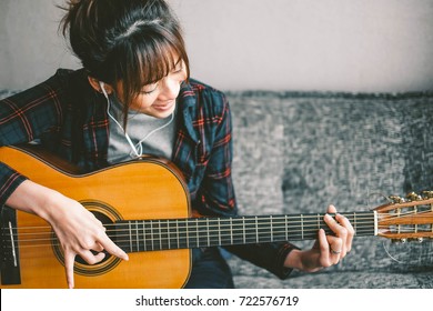 A Beautiful Asian Woman Smile While Playing Acoustic Guitar And Listening To Music,sitting On Sofa At Home