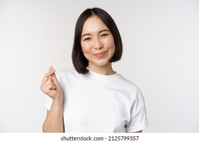 Beautiful Asian Woman Smiling, Showing Finger Hearts Gesture, Wearing Tshirt, Standing Against White Background