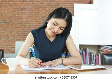 Beautiful Asian Woman Smiling And Writing A Notebook On Table